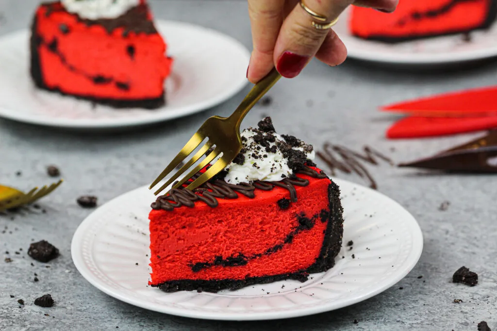 image of a slice of red velvet oreo cheesecake decorated with melted chocolate, whipped cream and crushed oreos