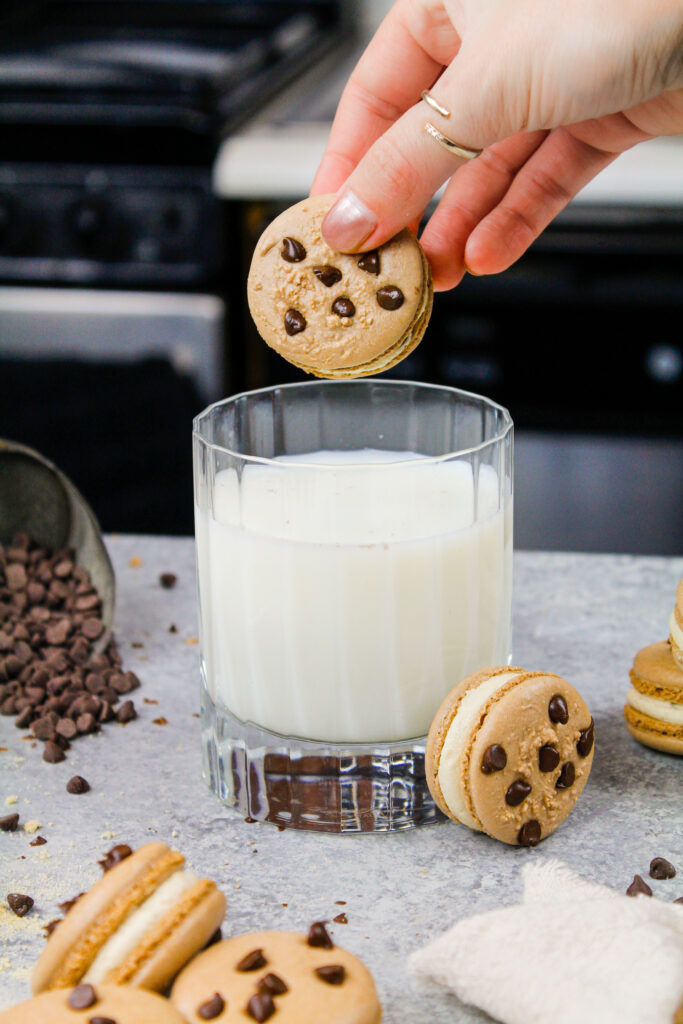 image of cookie dough macarons filled with cookie dough buttercream being dunked into a glass of milk