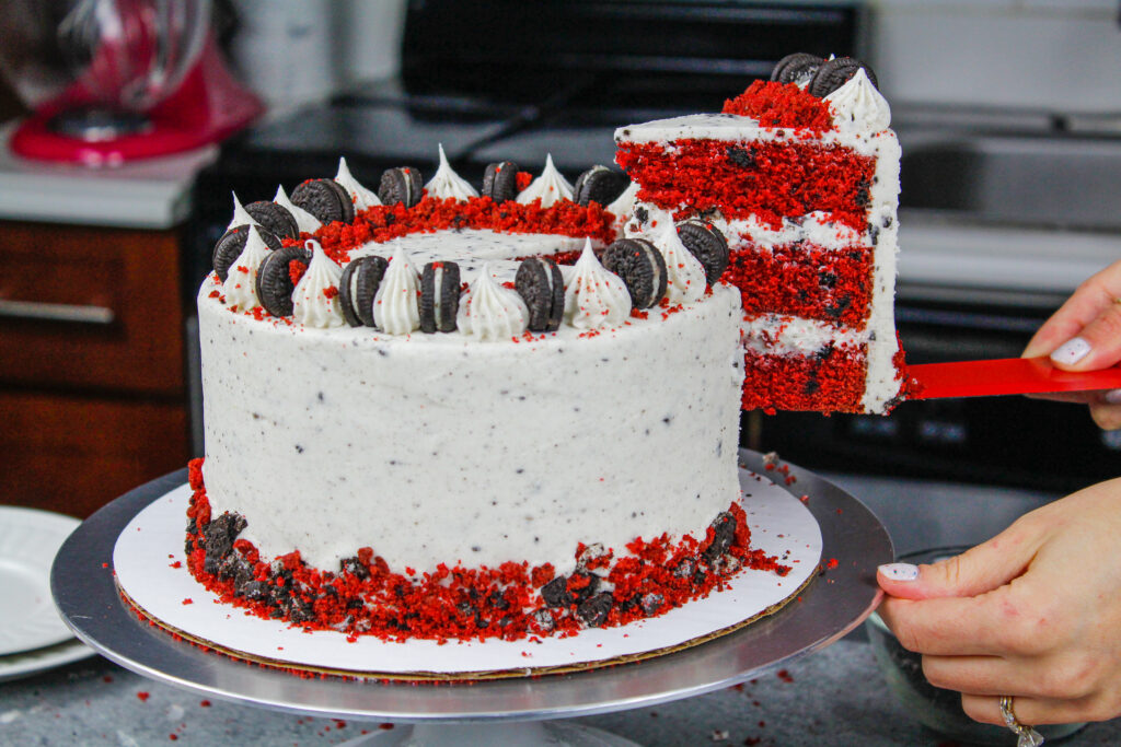 image of a red velvet oreo cake slice being pulled out of a cake that's frosted with oreo cream cheese frosting