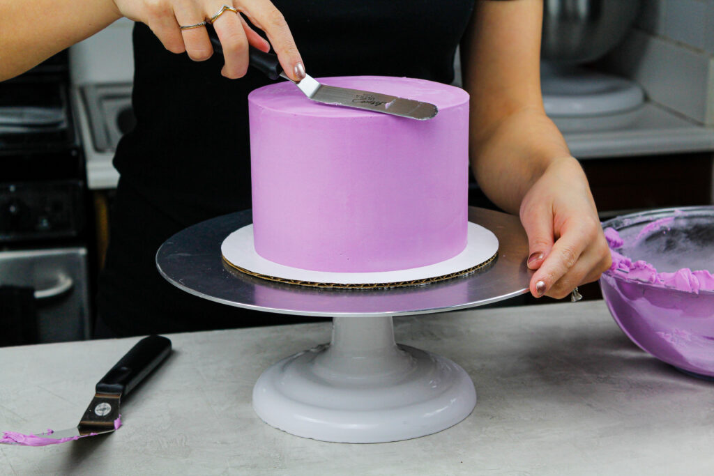 image of a cake being crumb coated in purple buttercream