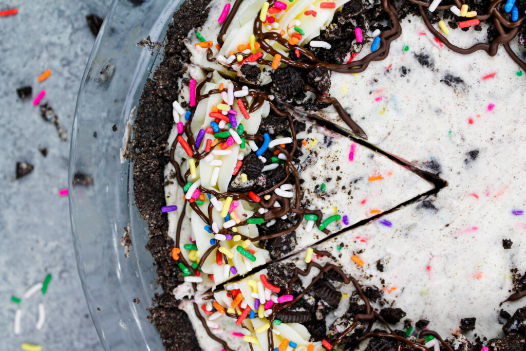 image of an oreo cream pie decorated with sprinkles and buttercream that's been sliced with a sharp knife to help remove the perfect first slice