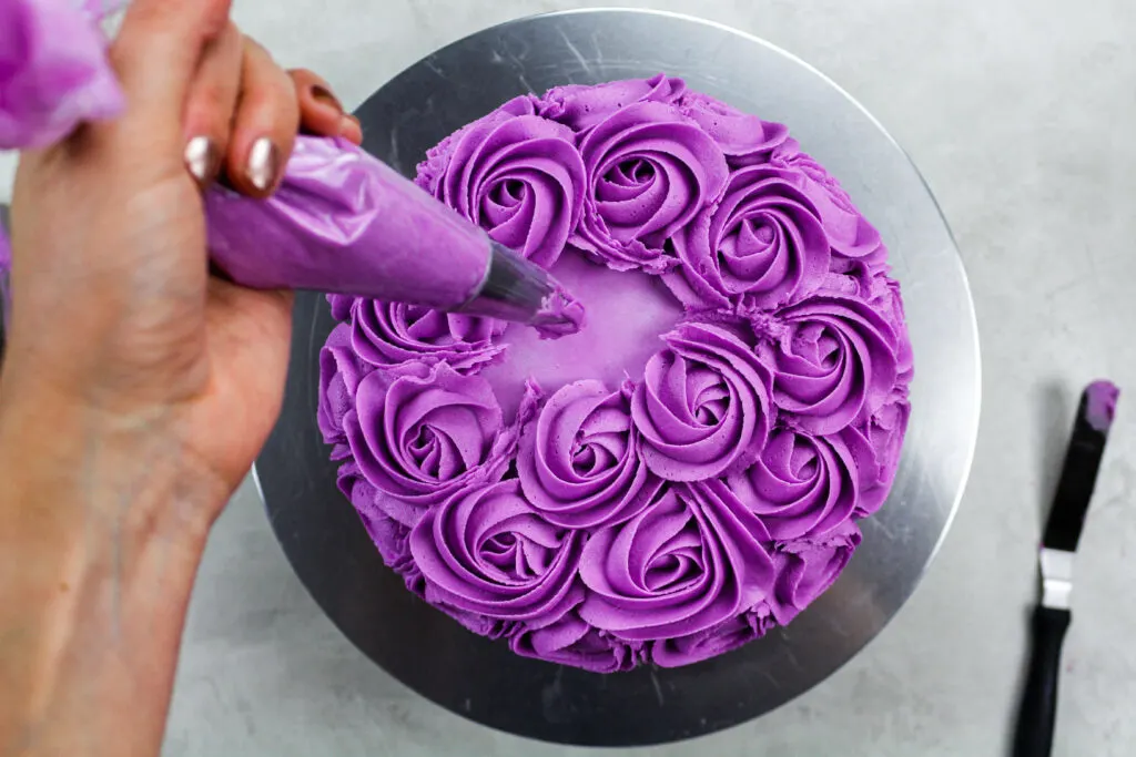 image a of a purple buttercream rosette being piped onto a cake