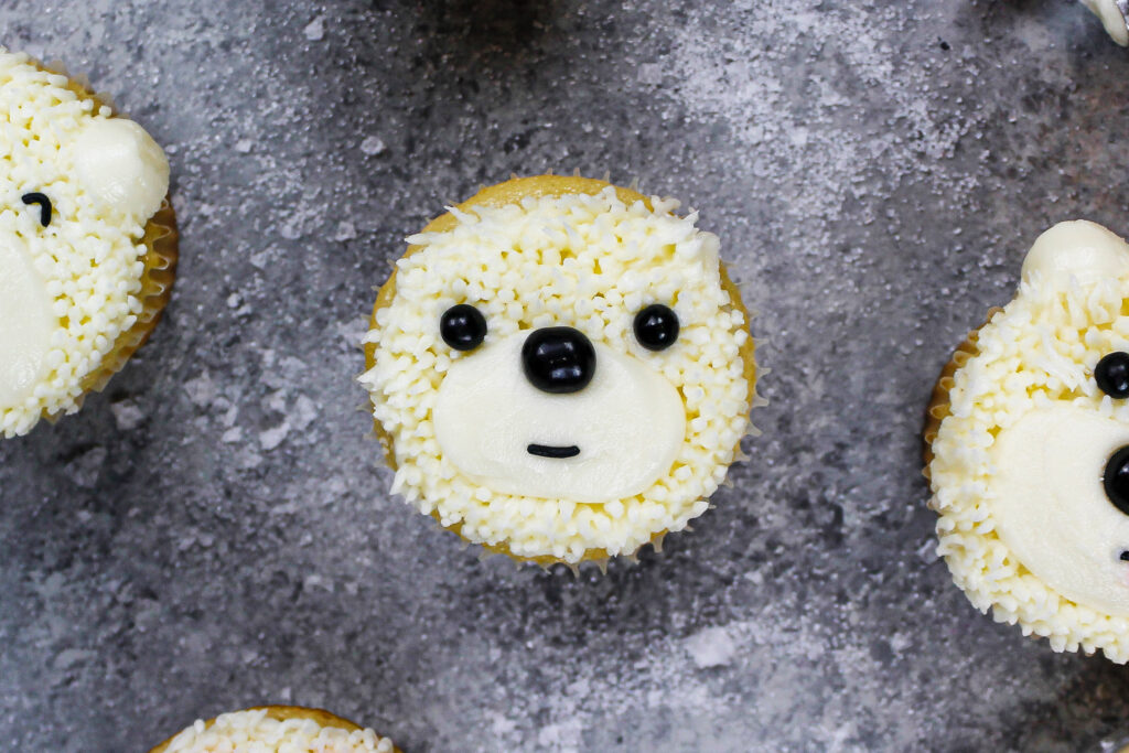 image of a polar bear cupcake being made with buttercream and black sprinkles for the face