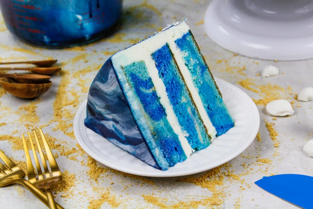 image of an ocean themed cake made with blue swirled cake layers and a pretty blue and white mirror glaze