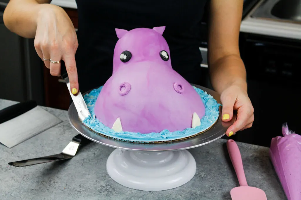 image of blue buttercream being added around a hippo cake to make it look like its head is peaking out of water
