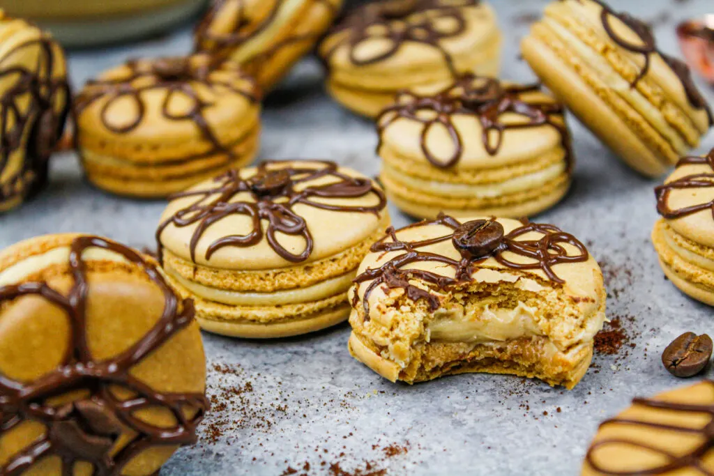 image of coffee macarons filled with coffee buttercream that have bitten into to show their full, perfect shells that was shared as part of a macaron round up