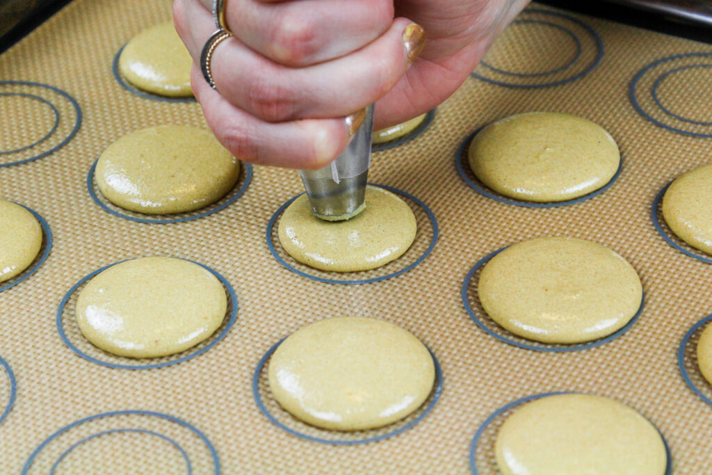 image of coffee macaron shells being piped onto a silicone mat