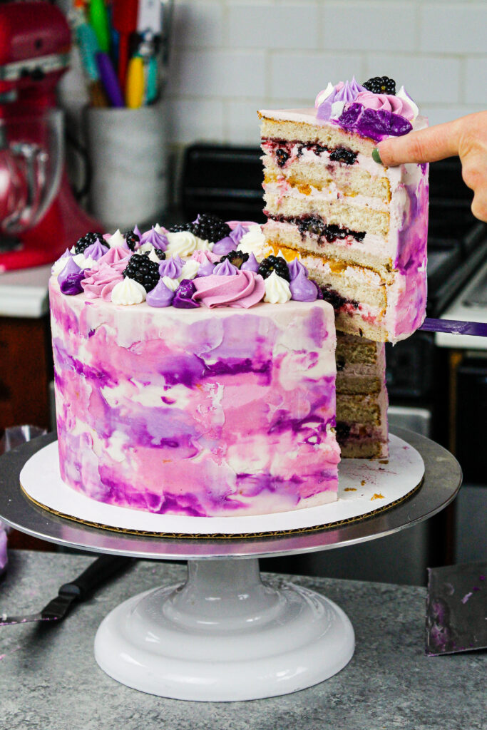 image of a beautiful blackberry and peach layer cake that's been cut into to show it's peach and blackberry filling
