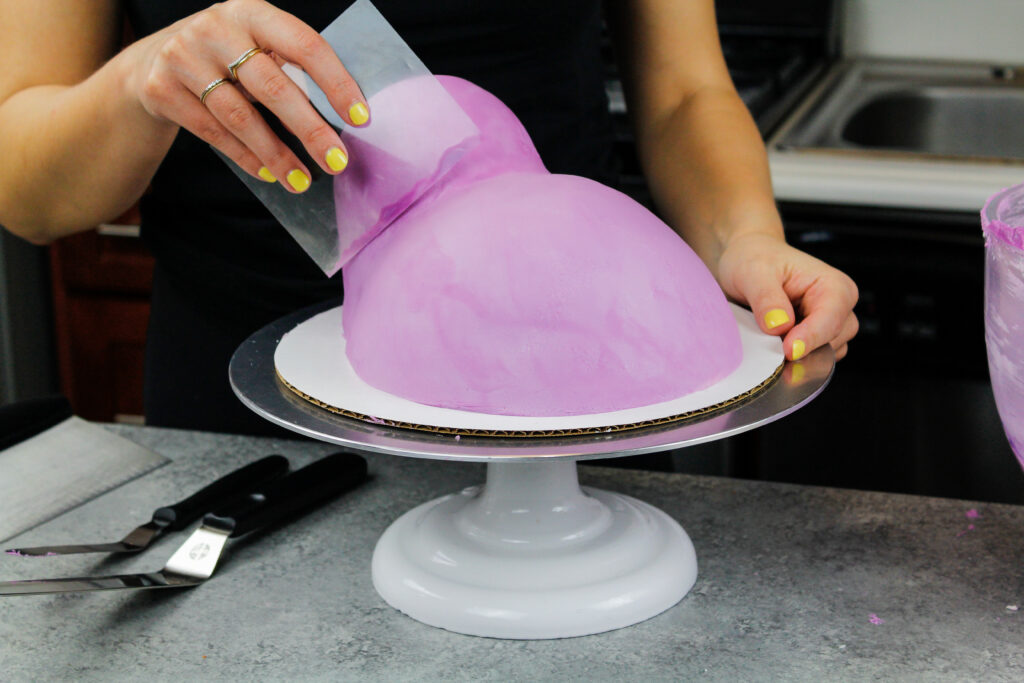 image of purple frosting being smoothed onto a cake with an acetate sheet