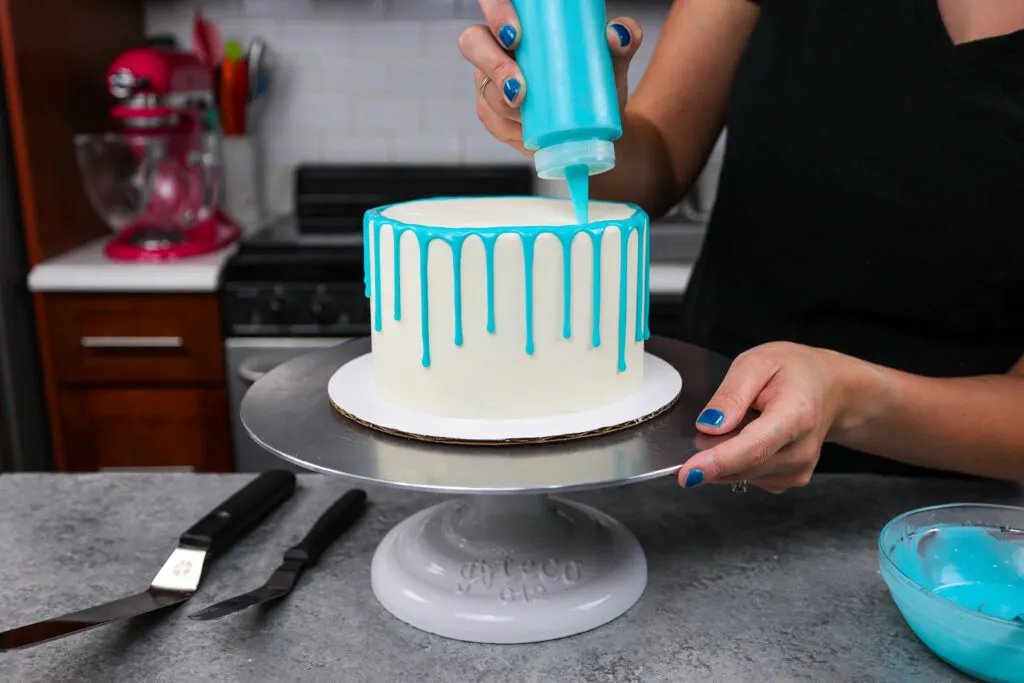 image of blue drips being added to a buttercream cake with a plastic squirt