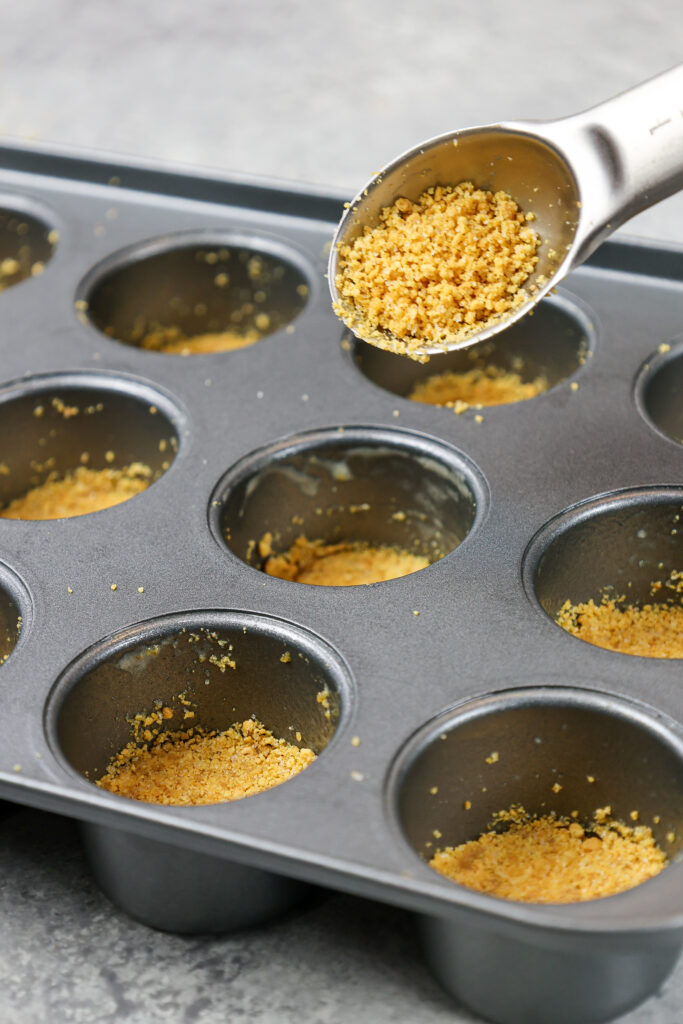 image of graham cracker crumbs being pressed into a mini cheesecake pan to make mini cheesecakes