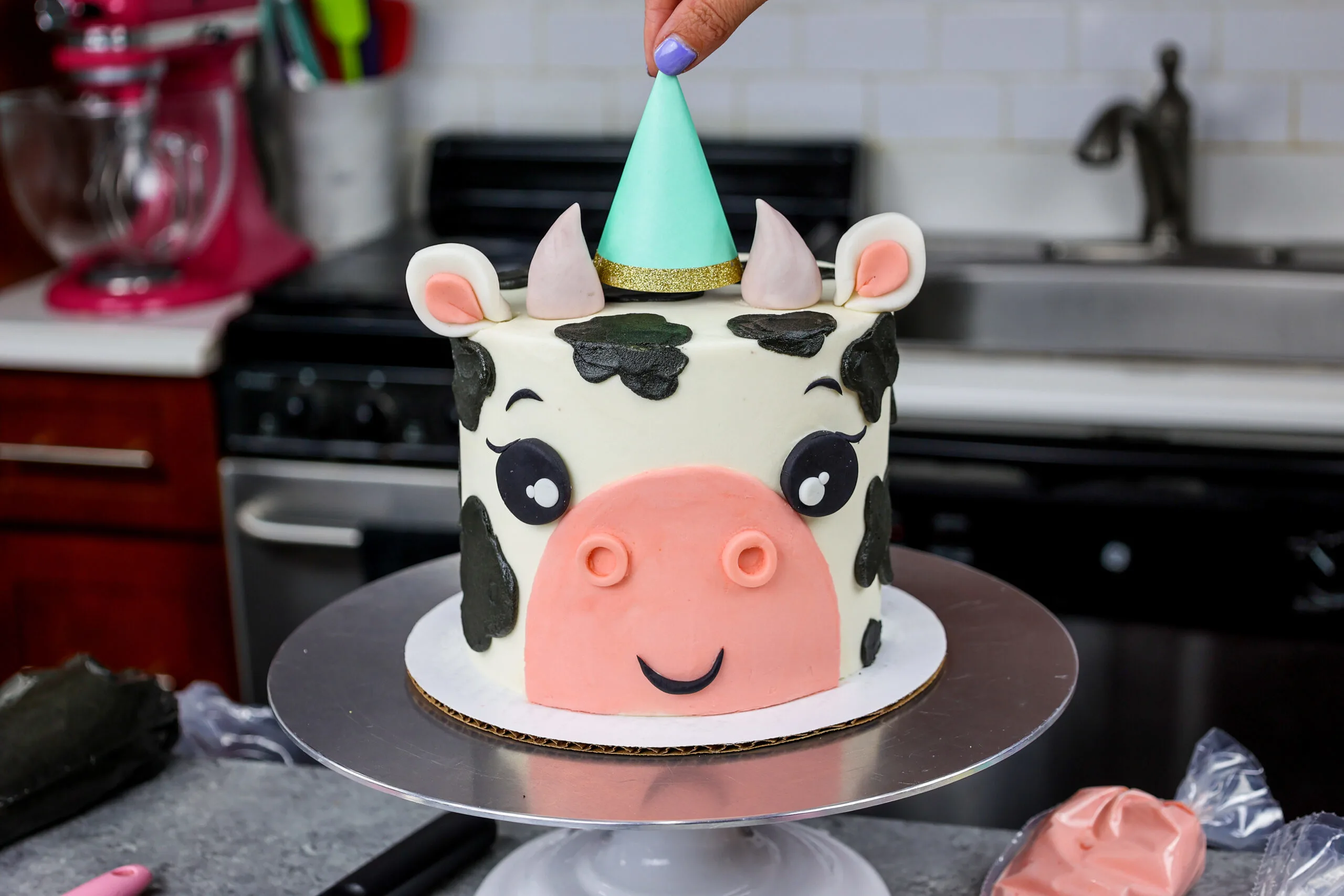 image of an adorable cow birthday cake made with marbled chocolate and vanilla cake layers and topped with a cute little party hat