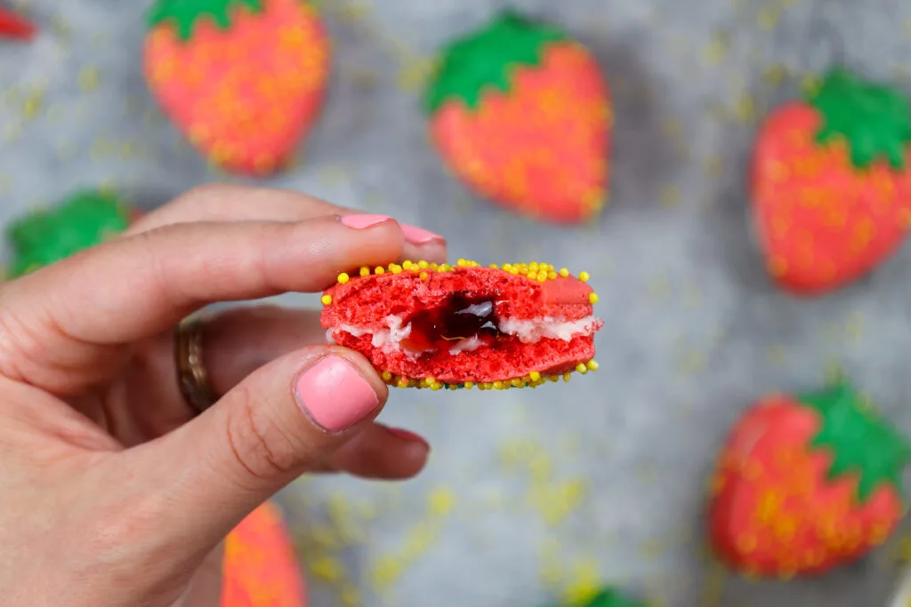 image of a strawberry macaron that's been bitten into to show it's buttercream and strawberry jam filling