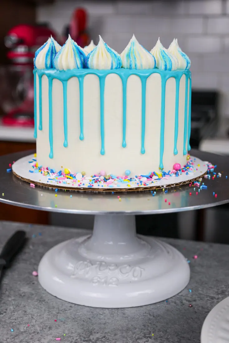 image of a blue drip cake decorated with pretty sprinkles and frosting dollops