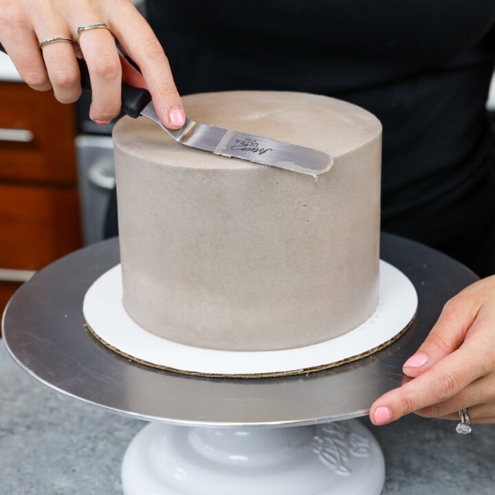image of a cake being frosted with buttercream to have super smooth sides and sharp edges