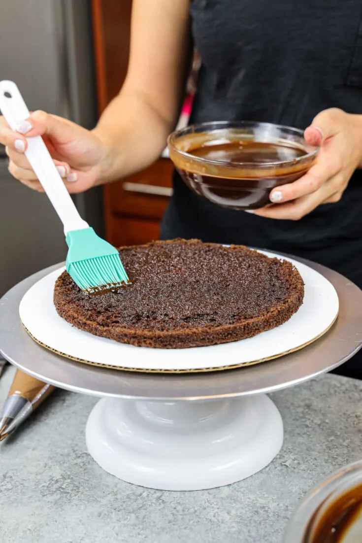 image of a chocolate cake layer being soaked with chocolate simple syrup