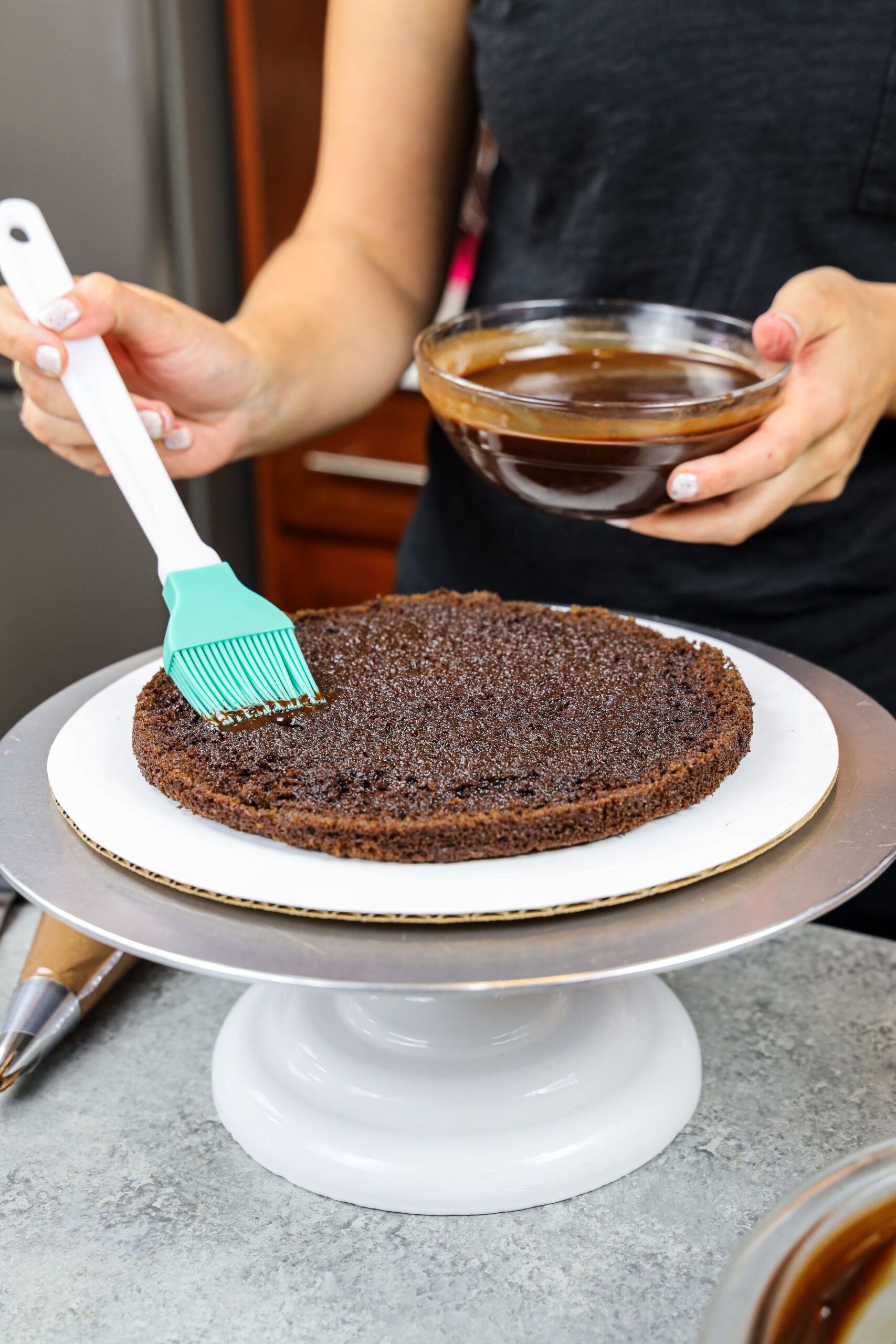 https://chelsweets.com/wp-content/uploads/2021/06/adding-chocolate-simple-syrup-onto-chocolate-cake-layer-vert-scaled.jpg