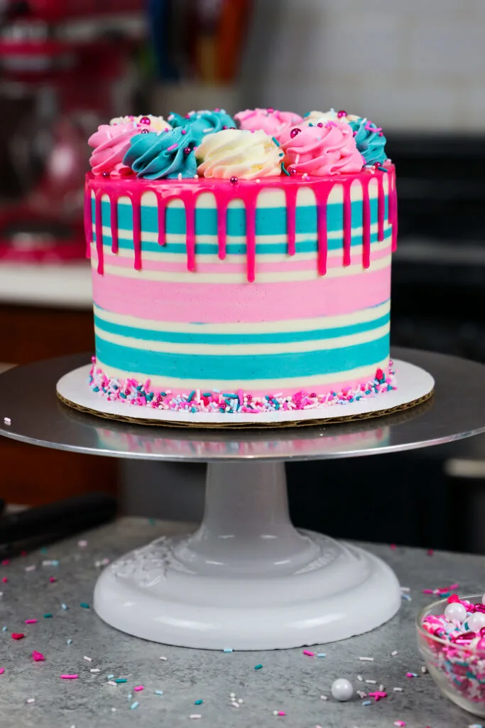 image of a gluten free funfetti cake that's been decorating with buttercream stripes and a pink drip