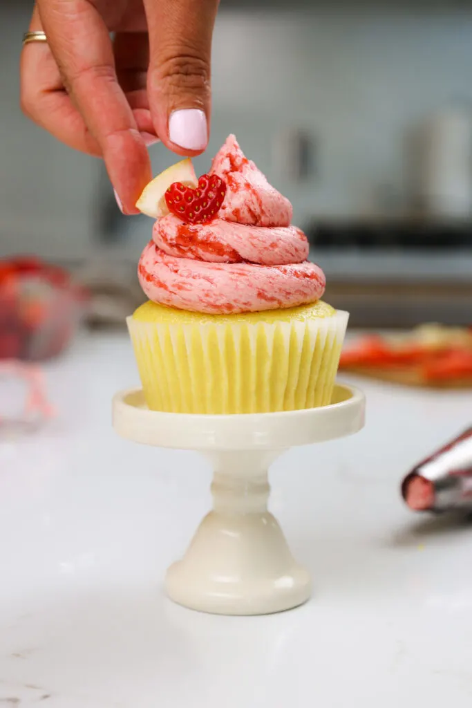 image of a strawberry lemonade cupcake being garnished with a cute little heart shaped strawberry cutout