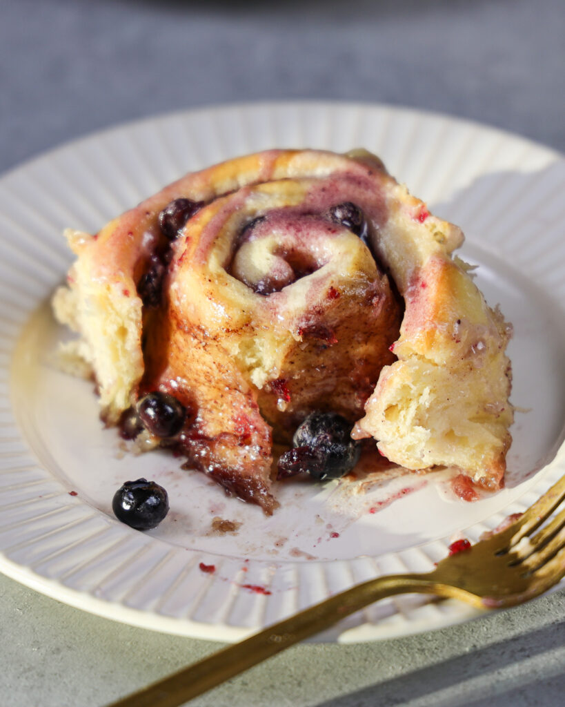 image of a blueberry cinnamon roll on a plate that's been cut into to show how soft and fluffy it is