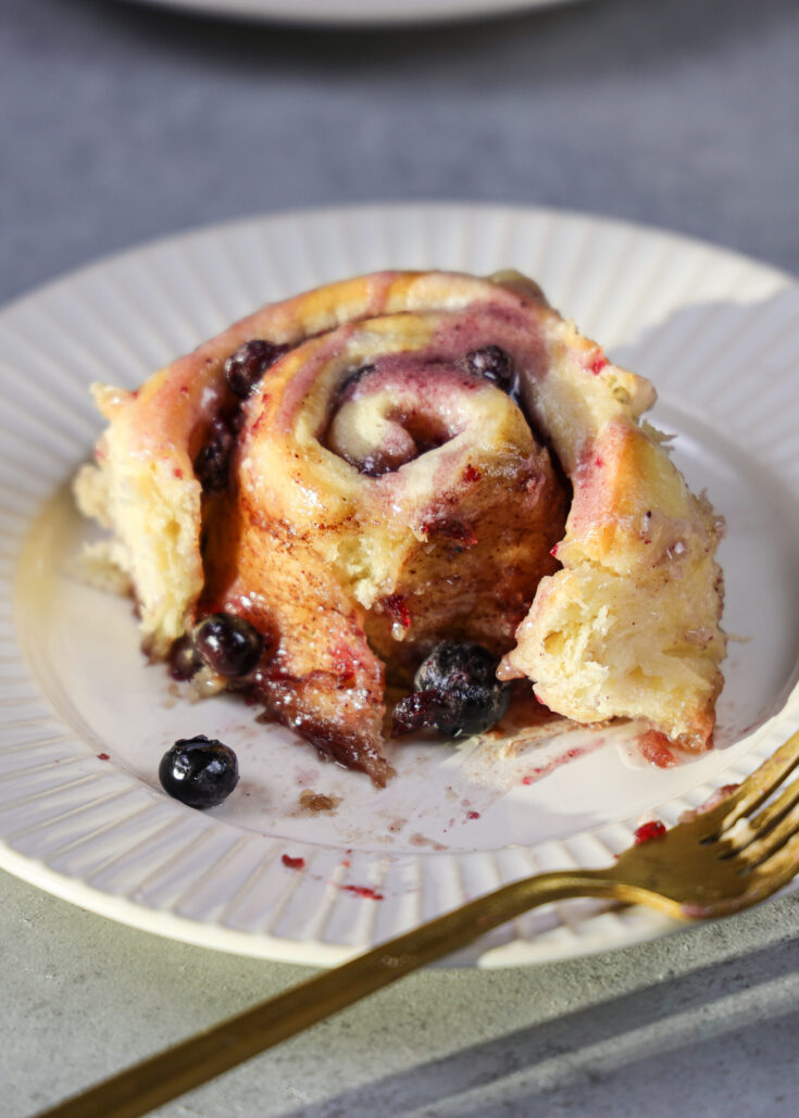 image of a blueberry cinnamon roll on a plate that's been cut into to show how soft and fluffy it is