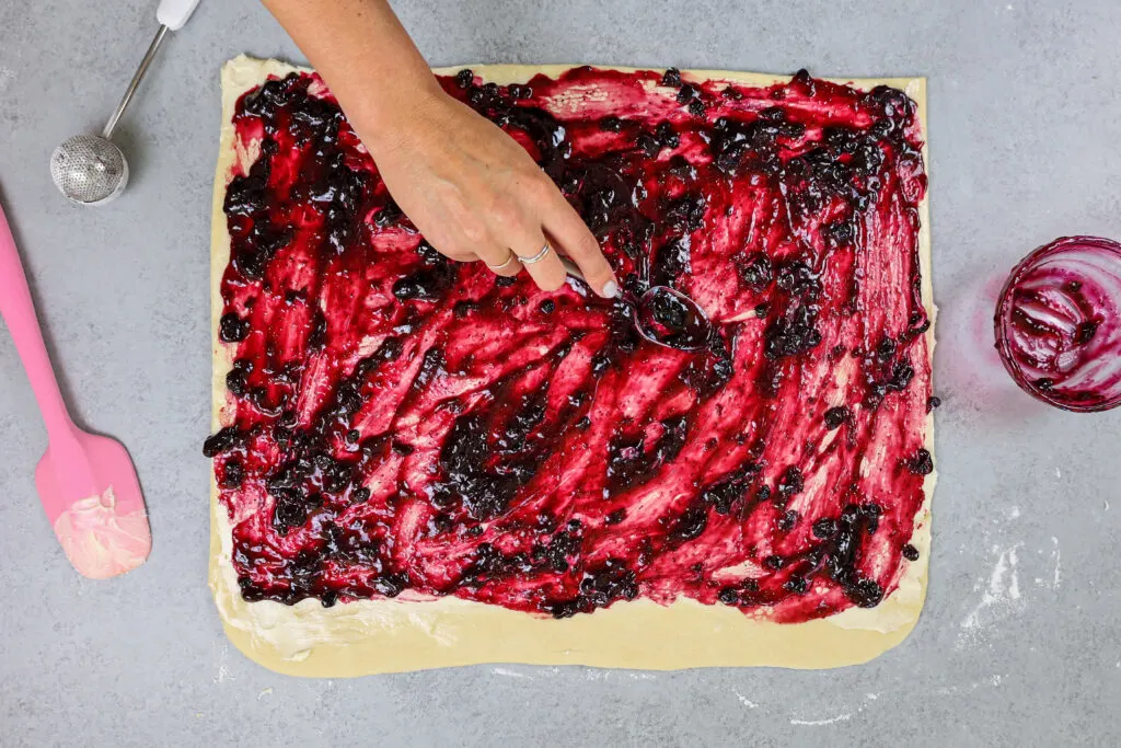 image of blueberry jam being spread onto cinnamon roll dough