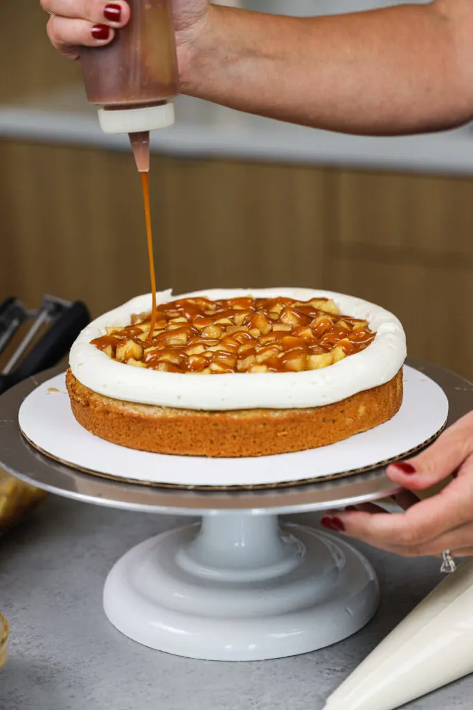 image of homemade caramel being drizzled on the filling of a salted caramel apple cake