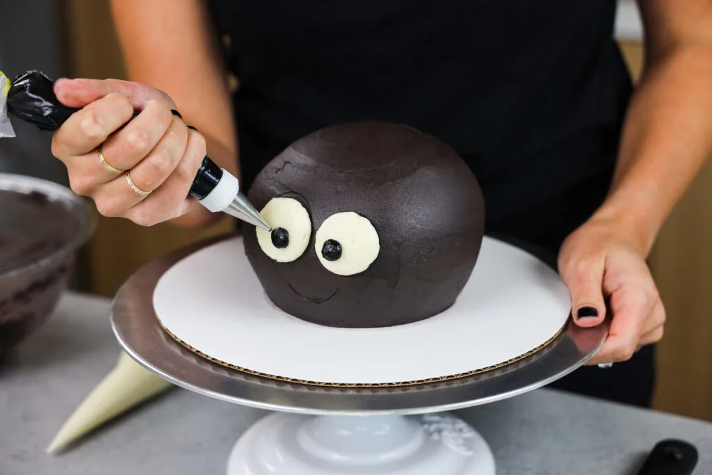 image of eyes being piped onto a cake to make a cute halloween spider cake