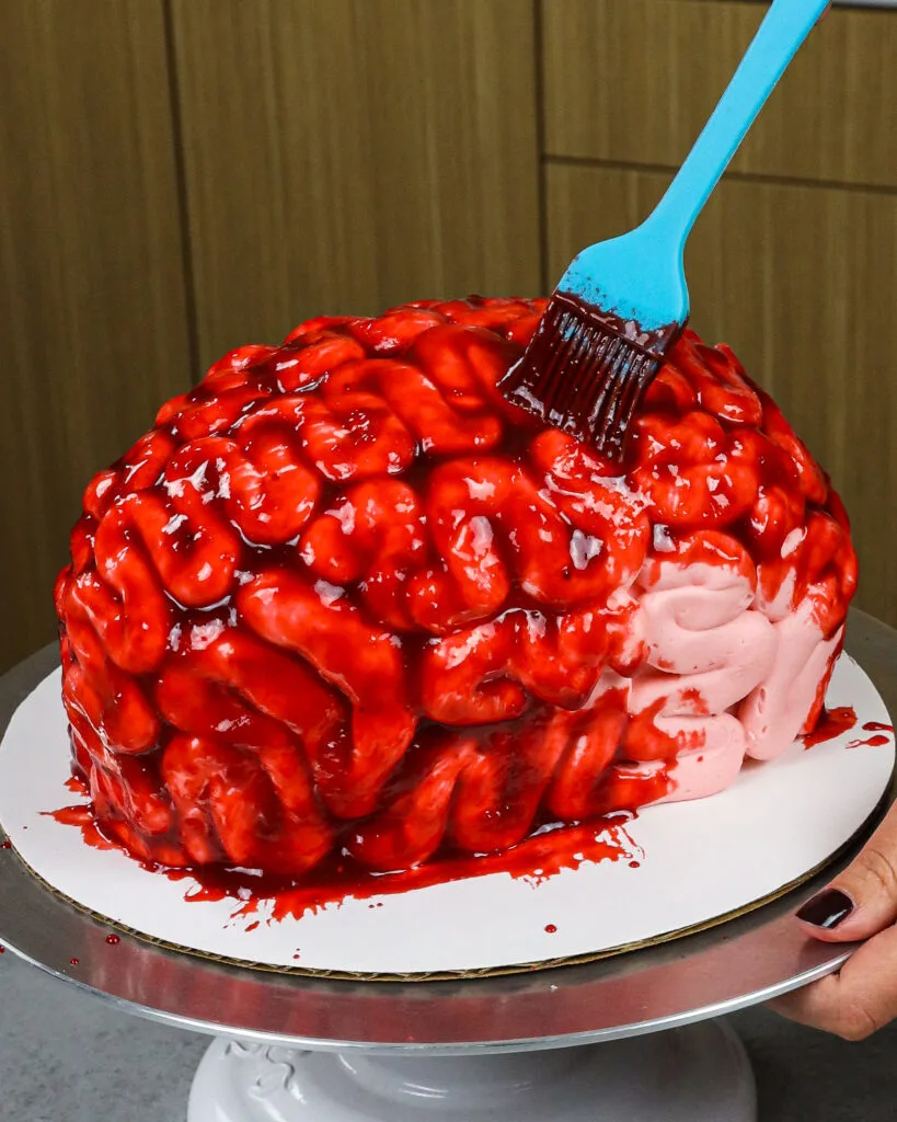 image of edible fake blood made with raspberry jam being brushed onto a brain cake for Halloween
