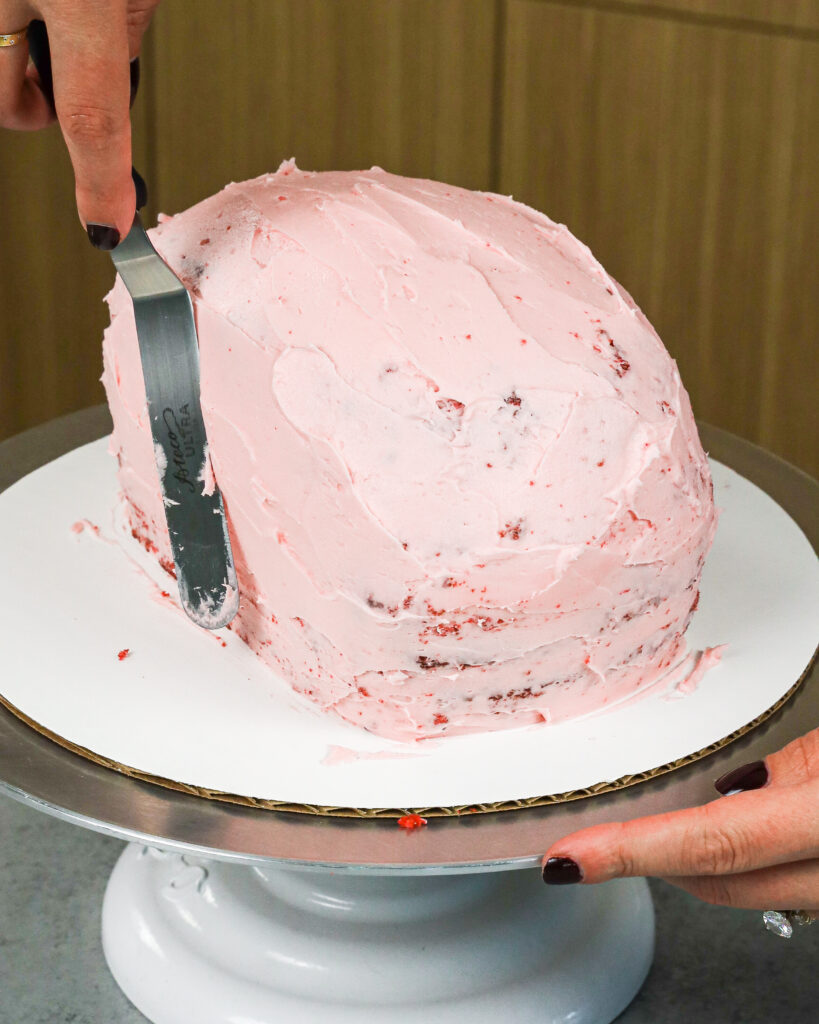 image of a red velvet cake being crumb coated with pink cream cheese frosting to make a brain cake for halloween