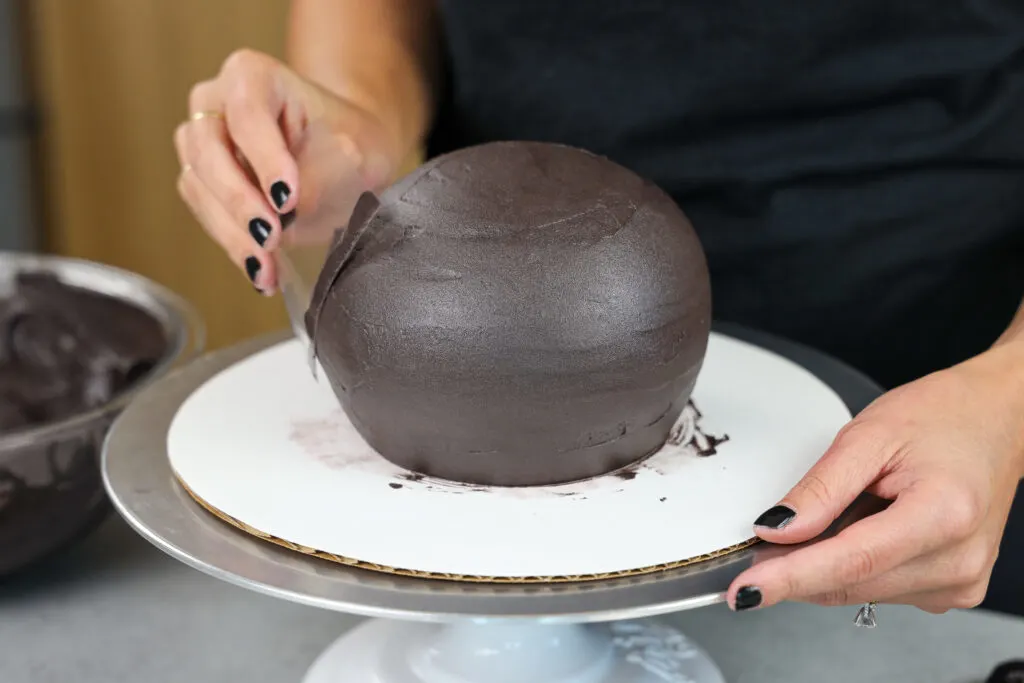 image of black chocolate buttercream being smoothed on a spherical cake