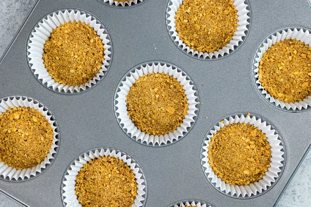 image of a cinnamon graham cracker crust being made in a muffin tin to make mini pumpkin cheesecake