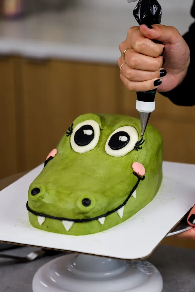 image of frosting eyelashes being piped onto a crocodile cake