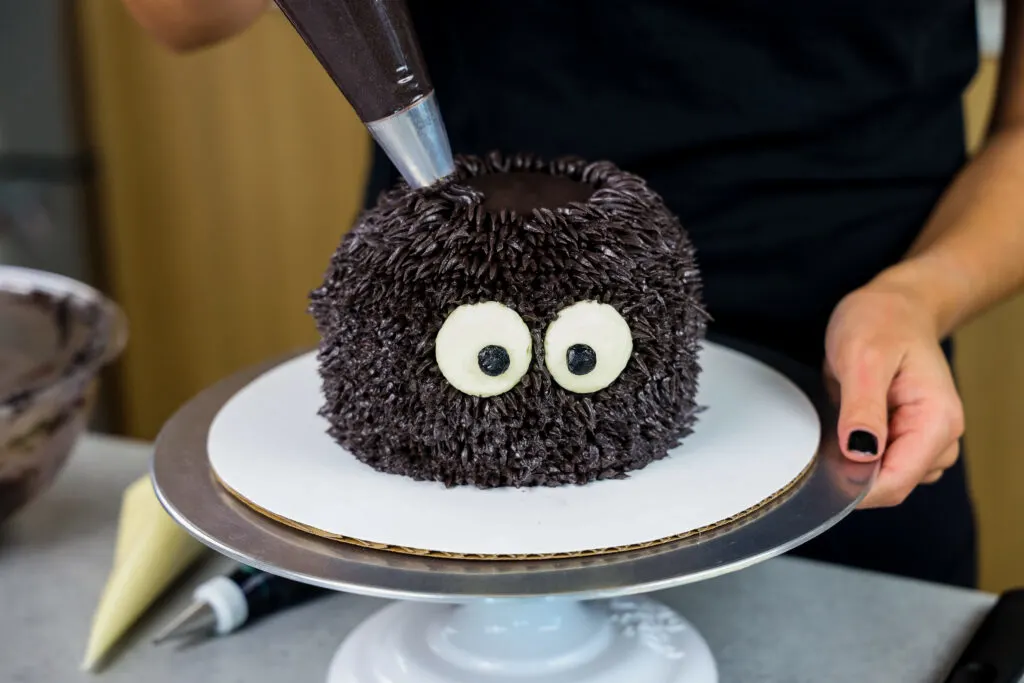 image of black buttercream being piped onto a spider cake to make it look cute and furry