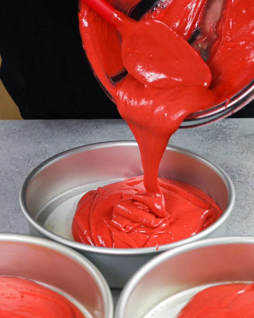 image of red velvet cake batter being poured into an 8 inch cake pan