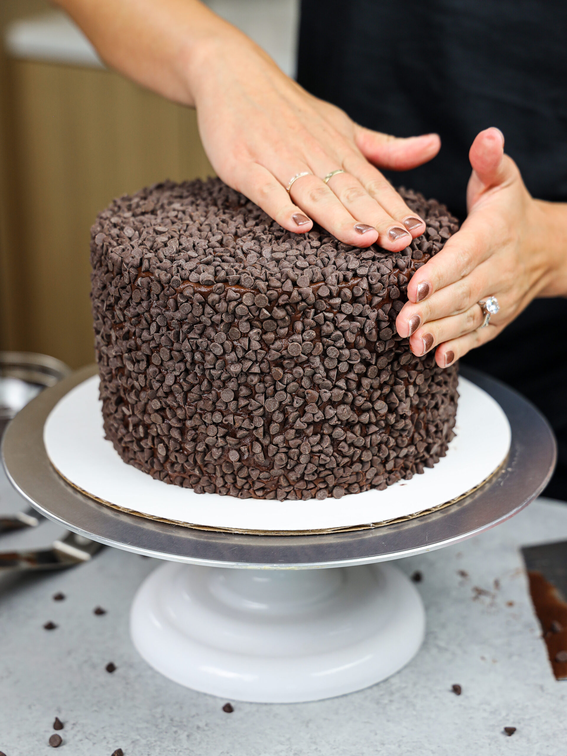 image of a dark chocolate cake being covered with mini chocolate chips