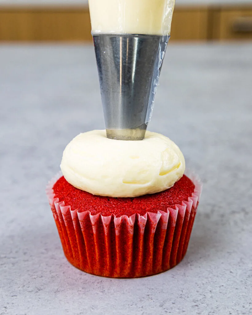 image of buttercream being piped onto a red velvet cupcake with a large round piping tip