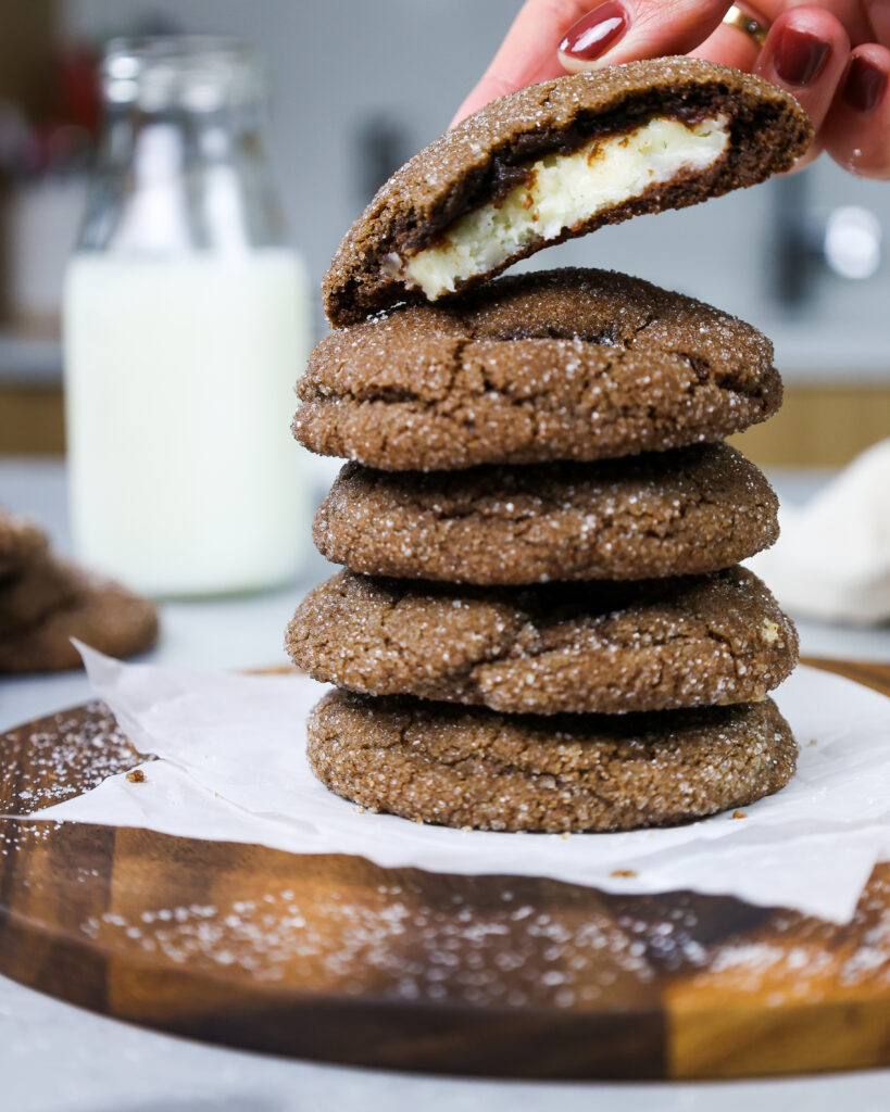 image of a chocolate cheesecake cookie being placed on top of a stack of cookies next to a bottle of milk