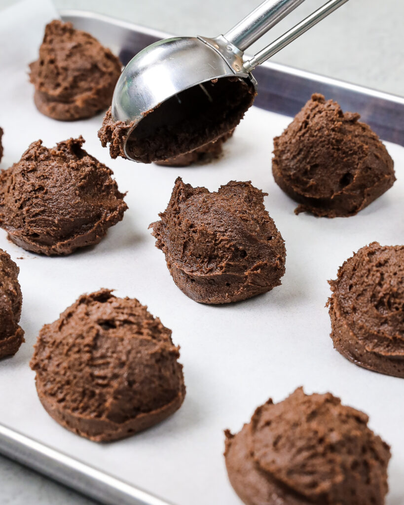 image of chocolate cookie batter being scooped and placed on a lined baking sheet to be chilled in the fridge