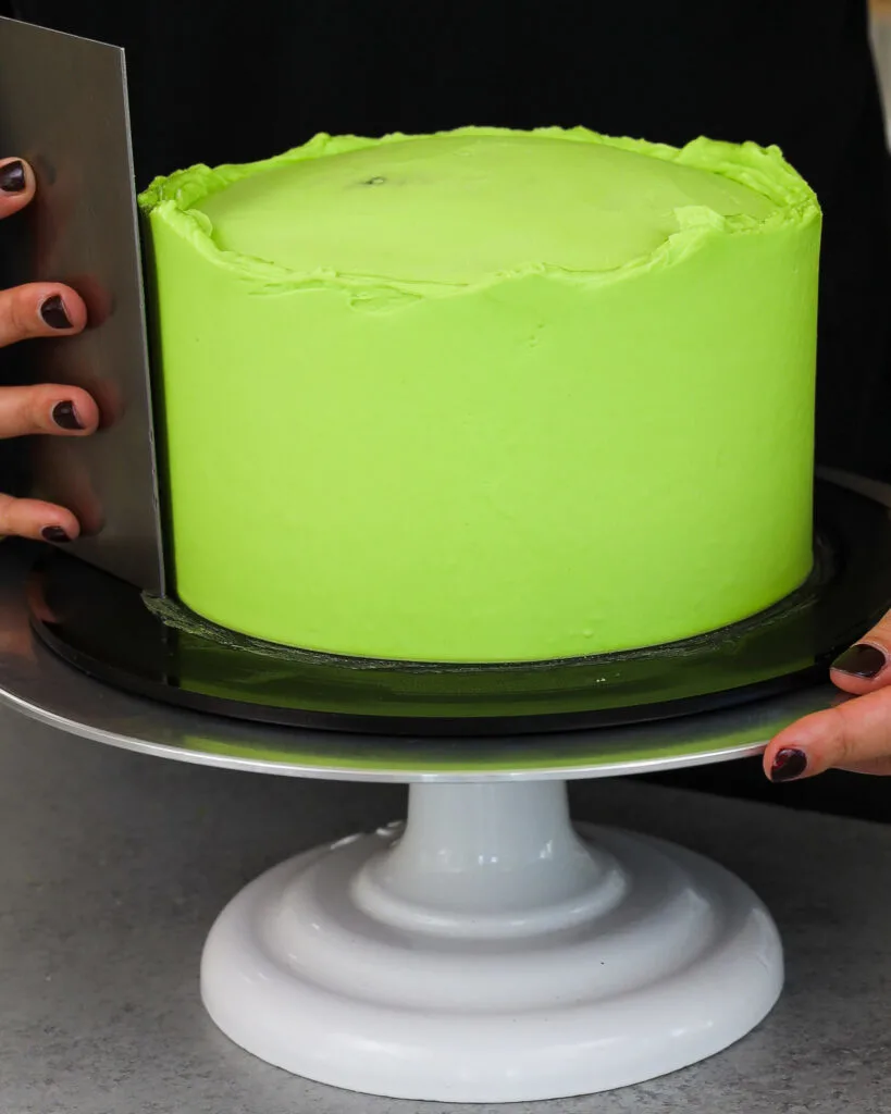 image of a cake being frosted with a second thicker layer of bright green American buttercream