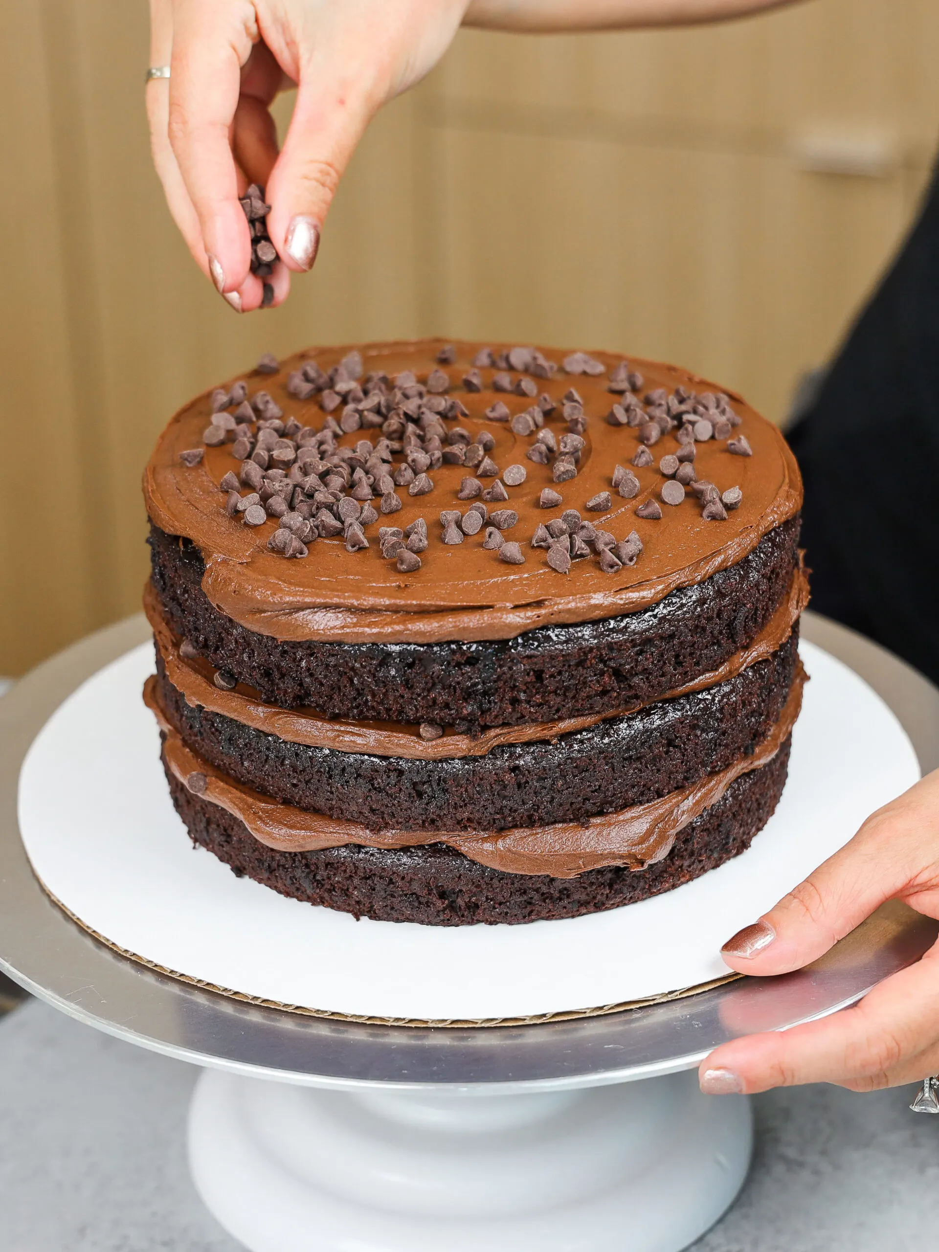 image of death by chocolate cake being assembled with dark chocolate frosting and mini chocolate chips
