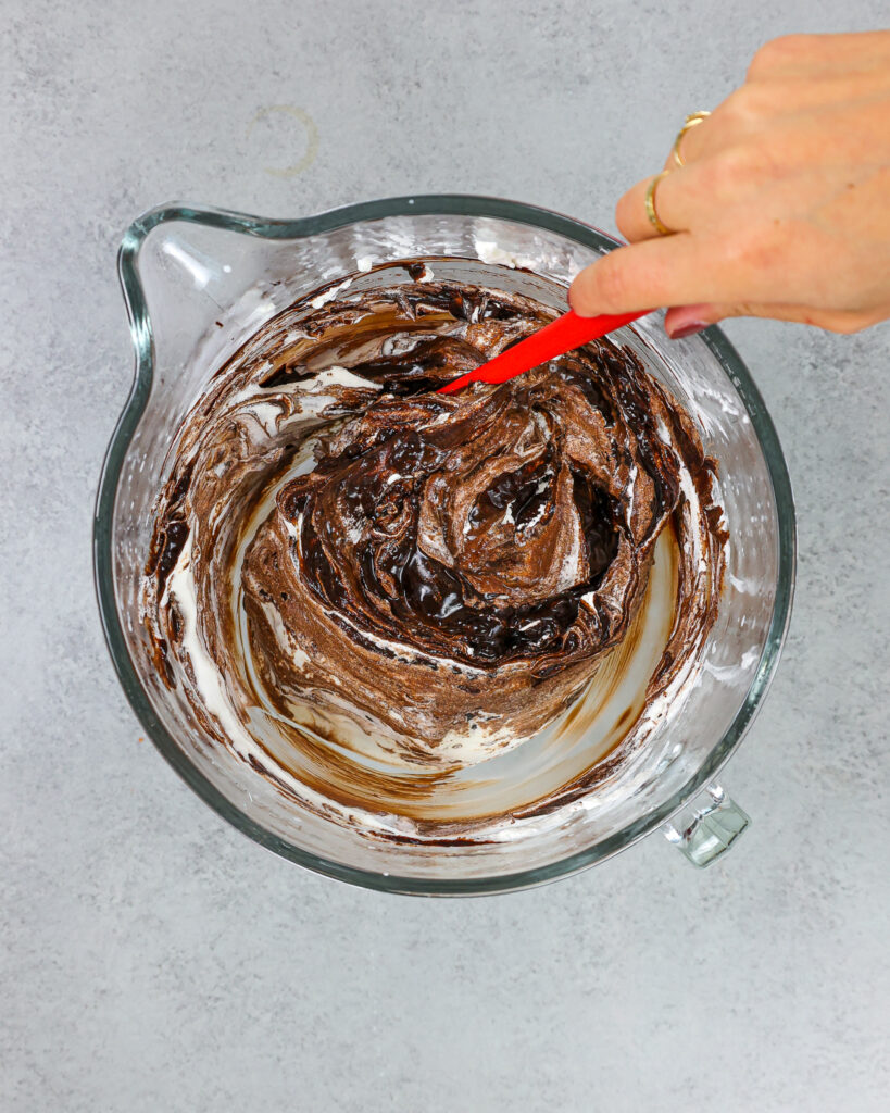 image of melted chocolate being folded into whipped cream to make a chocolate mousse cake filling