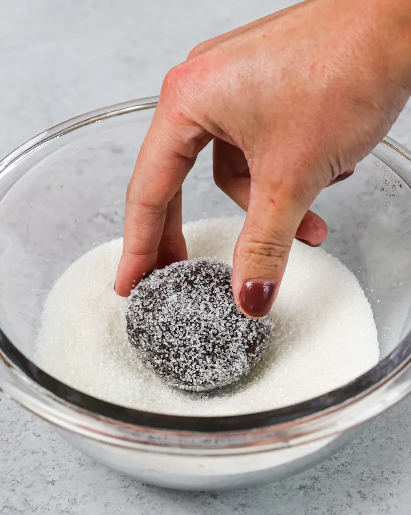 image of cheesecake filled chocolate cookies being tossed in granulated sugar