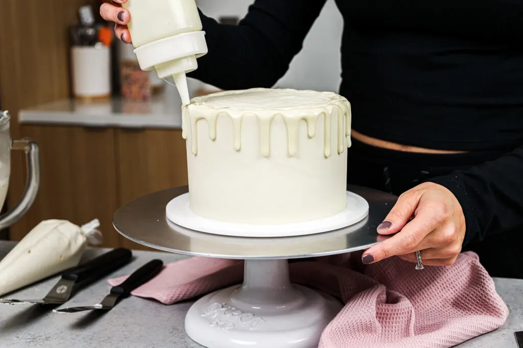 image of white chocolate ganache drips being added to a 6-inch cake with a plastic squirt bottle