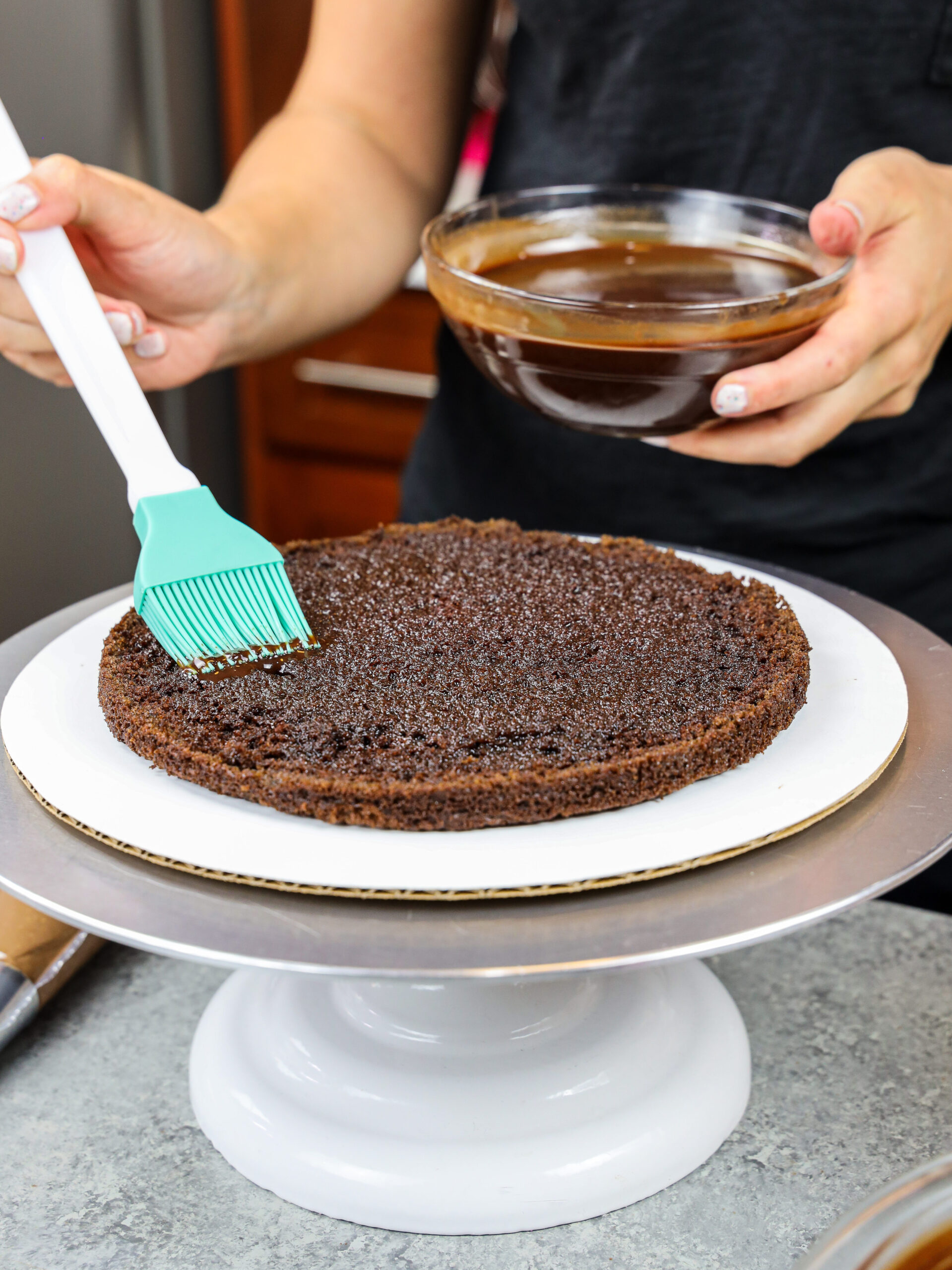 image of a chocolate cake layer being soaked with chocolate simple syrup