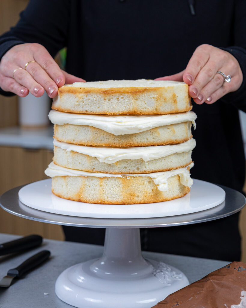 image of vanilla cake layers being stacked with buttercream frosting to make a layer cake
