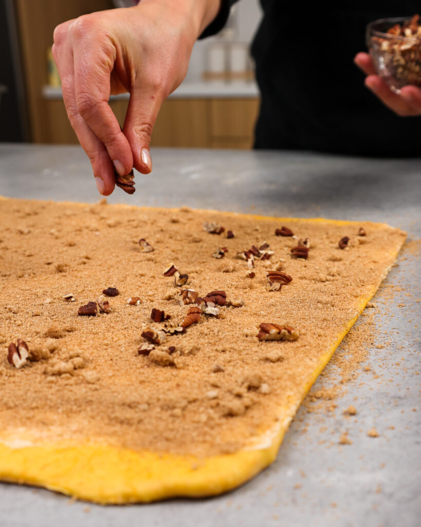 image of toasted pecans being added into the filling of a carrot cake cinnamon roll