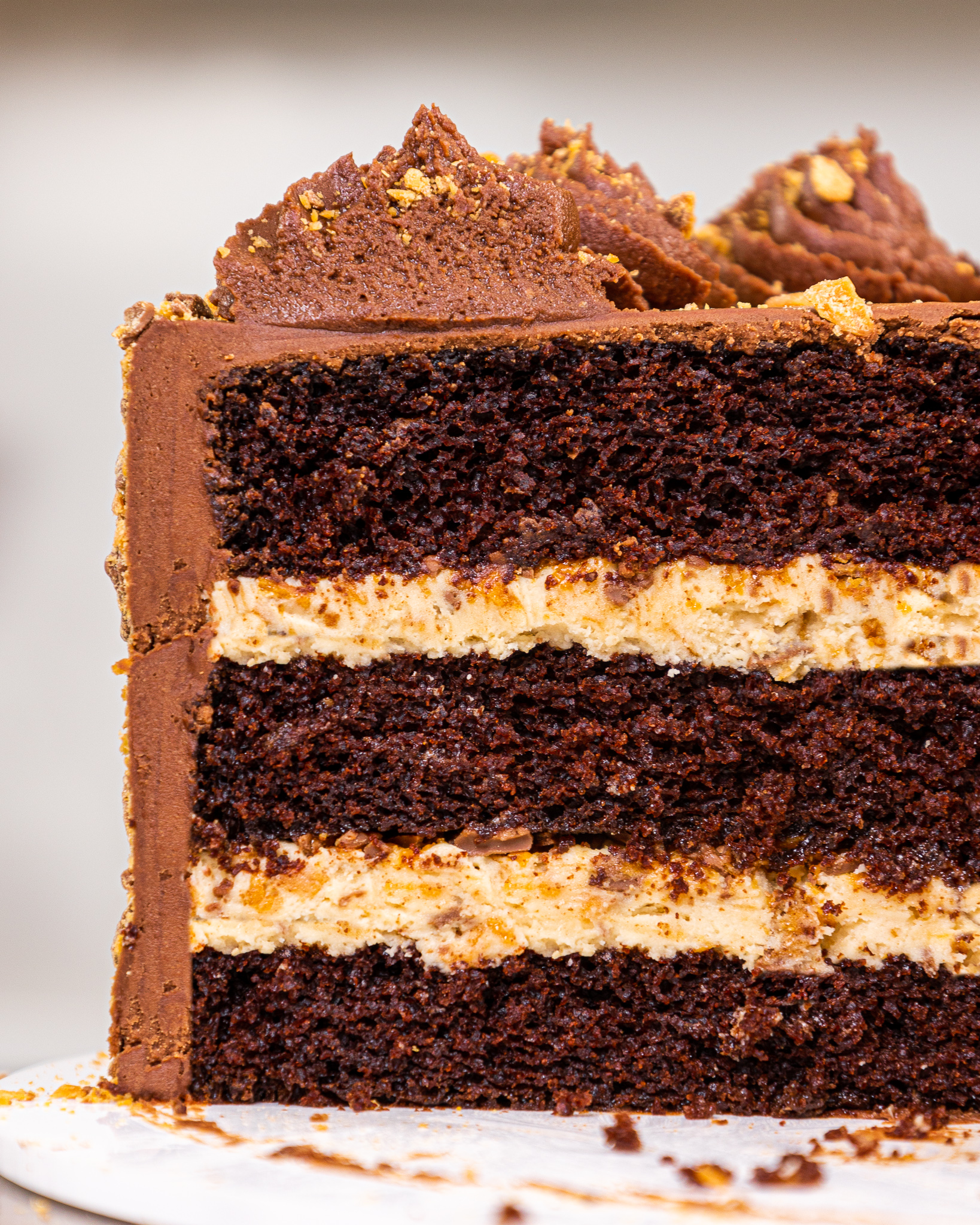 image of a butterfinger cake that's been cut into to show its crunchy peanut butter butterfinger filling and tender chocolate cake layers