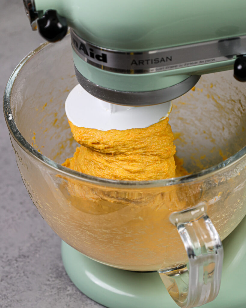 image of carrot cake cinnamon roll dough being made in a stand mixer using a dough hook