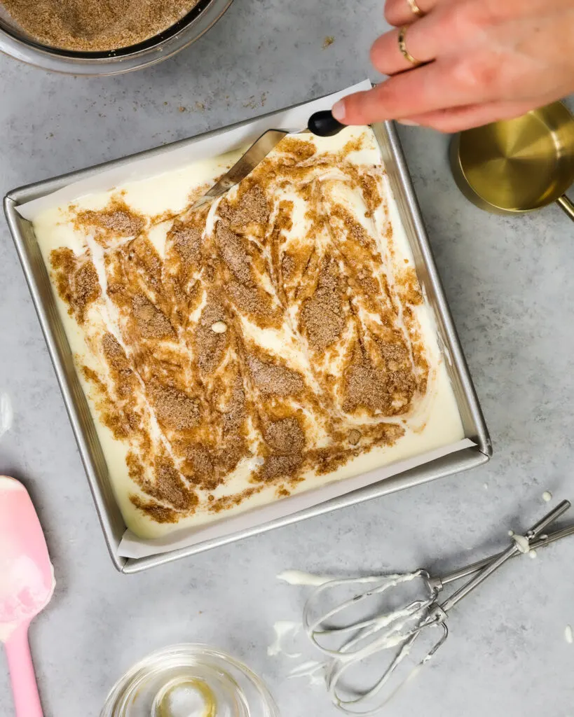 image of a pan of snickerdoodle cheesecake bars that are being swirled together with cinnamon sugar